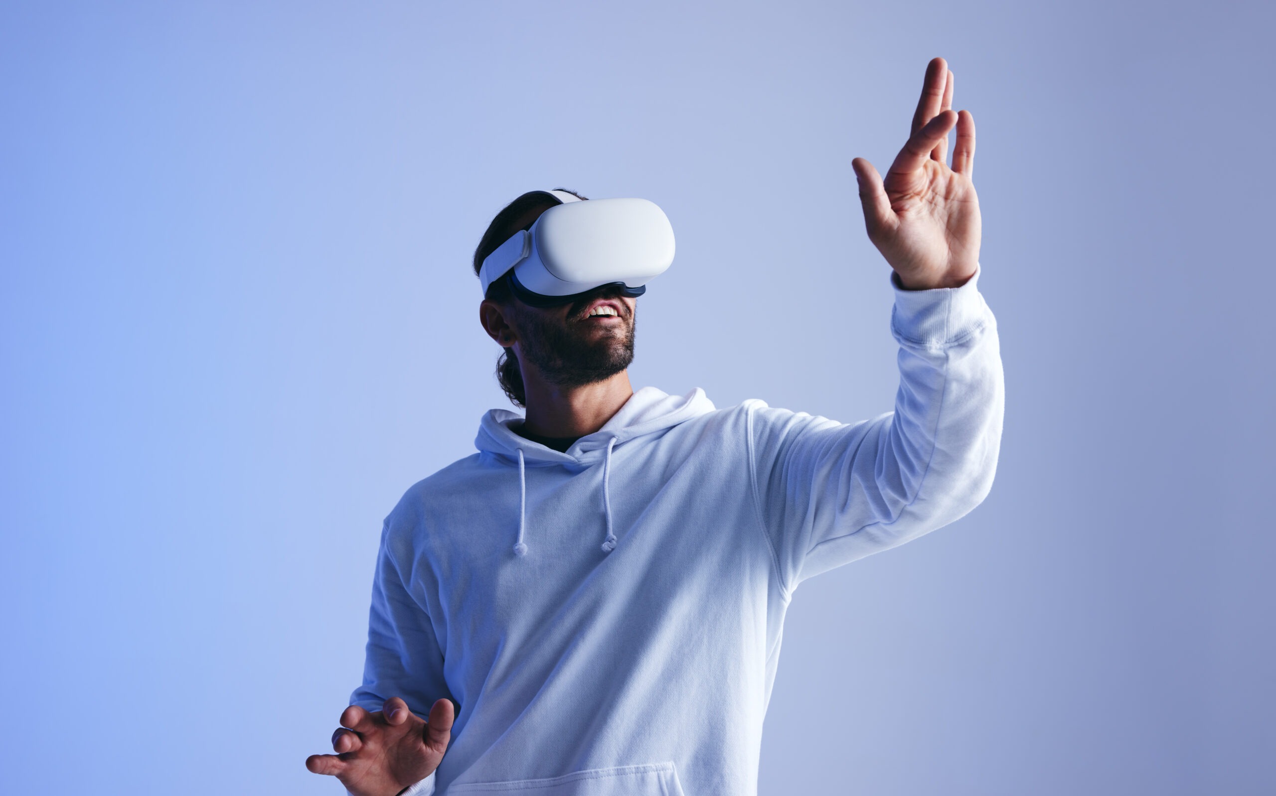 Happy young man touching virtual space with his hand. Cheerful young man experiencing a fun 3D simulation. Young man interacting with the metaverse using virtual reality goggles.